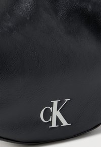 Μαύρη υφή δέρματος με το λευκό λογότυπο "cK" τυπωμένο κοντά στην κάτω δεξιά γωνία.