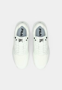 Egy fehér Fila tornacipő pár fűzőkkel, felülről nézve, egy sima világosszürke háttéren.