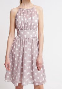 Šaty s puntíky v světle mauve barvě s bílými puntíky, halter výstřih, nařasený živůtek a přiléhavý pas. Lehká látka s volánovou sukní.