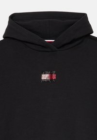Svart hettegenser med en liten, flerfarget rhinsteinlogo på brystet. Stoffet er mykt med en teksturert finish og snor i hetten.