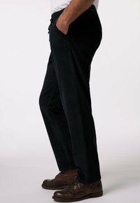 Pantalons en velours côtelé noirs avec une coupe décontractée, dotés de poches latérales et d'une taille élastique. Portés avec des chaussures marron à lacets.