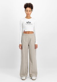 Hvit langermet crop top med "Alpha Industries" logo, sammen med løstsittende beige vanntette bukser. Hvit sneakers fullfører antrekket.
