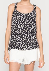 Black floral tank top with white daisies, featuring ruffled straps and a relaxed fit. Paired with distressed white shorts.