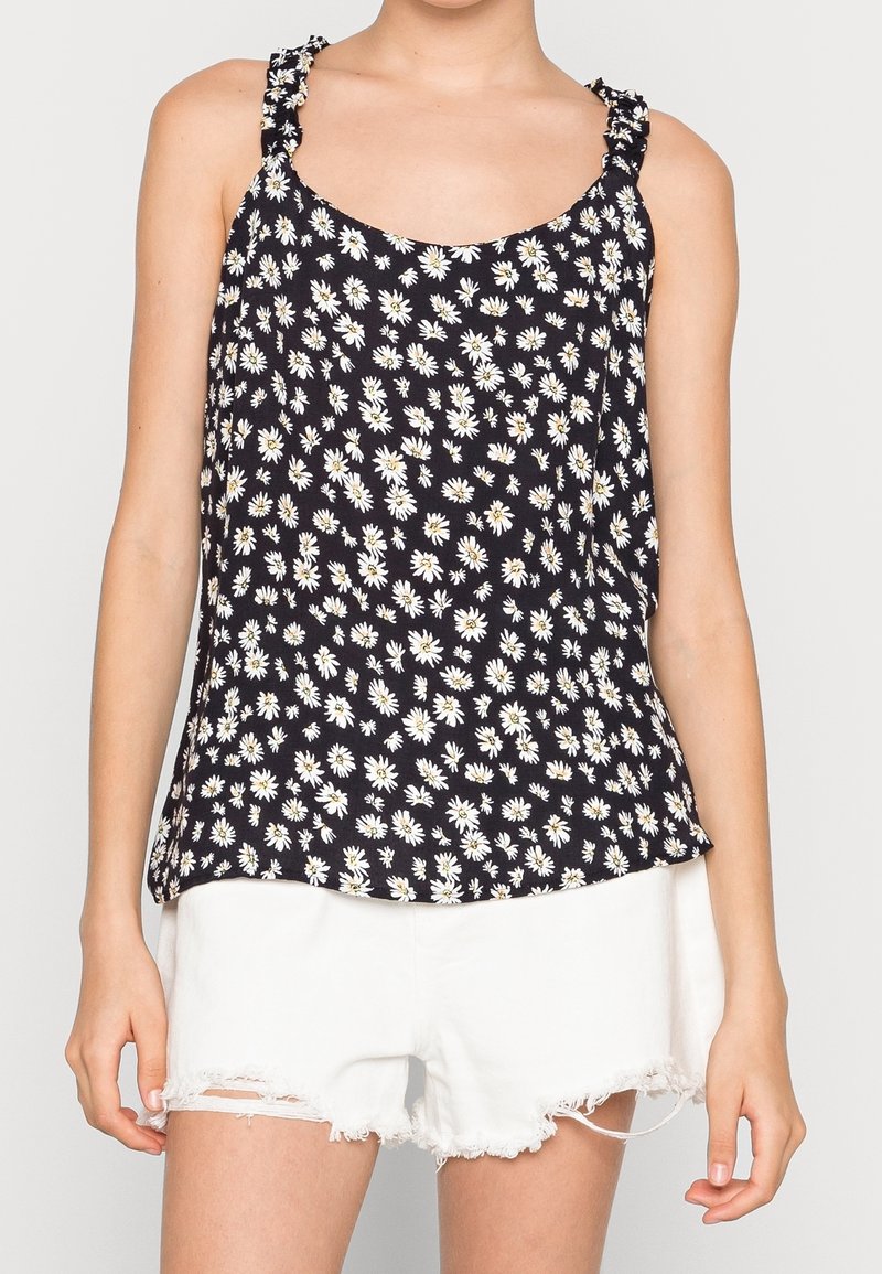 Black floral tank top with white daisies, featuring ruffled straps and a relaxed fit. Paired with distressed white shorts.