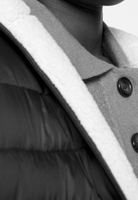 Doudoune avec une couche extérieure noire, dotée d'un col en laine grise, d'une doublure en polaire blanche et de boutons foncés. Accent mis sur la chaleur et la texture.