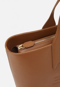 Braune Lederhandtasche mit glatter Textur, ausgestattet mit einem goldenen Reißverschluss und einer kleinen Innentasche. Robuste Griffe, minimalistisches Design.