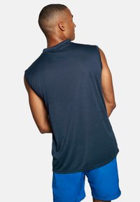 Ärmelloses navyblaues Sportshirt aus glattem Stoff, mit einem lässigen Schnitt und leichtem abgerundetem Saum, kombiniert mit blauen Shorts.