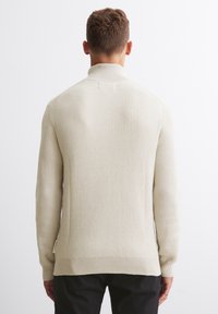 Helle beigefarbene, gerippte Strickjacke mit hohem Kragen und langen Ärmeln, ausgestattet mit einem geraden Saum und subtilen seitlichen Schlitzdetails.