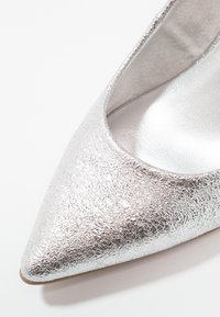 Chaussure plate argentée à bout pointu avec doublure intérieure lisse et semelle beige visible à la pointe.