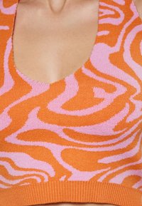 Pleteni halter top z oranžno in roza zebra vzorcem, z okroglim izrezom in teksturiranim rebrastim robom. Mehka, raztegljiva tkanina.