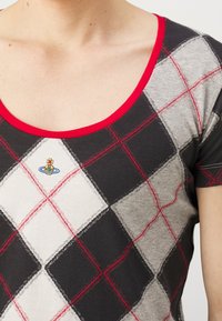 Close-up of a person wearing a black, gray, and white argyle patterned shirt with red lines and a red neckline trim.