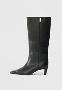 Schwarze Lederstiefelette bis zum Knie mit spitzem Zeh und kleinem Absatz. Hat ein elegantes Design mit goldenen Akzenten. Glatte Textur.