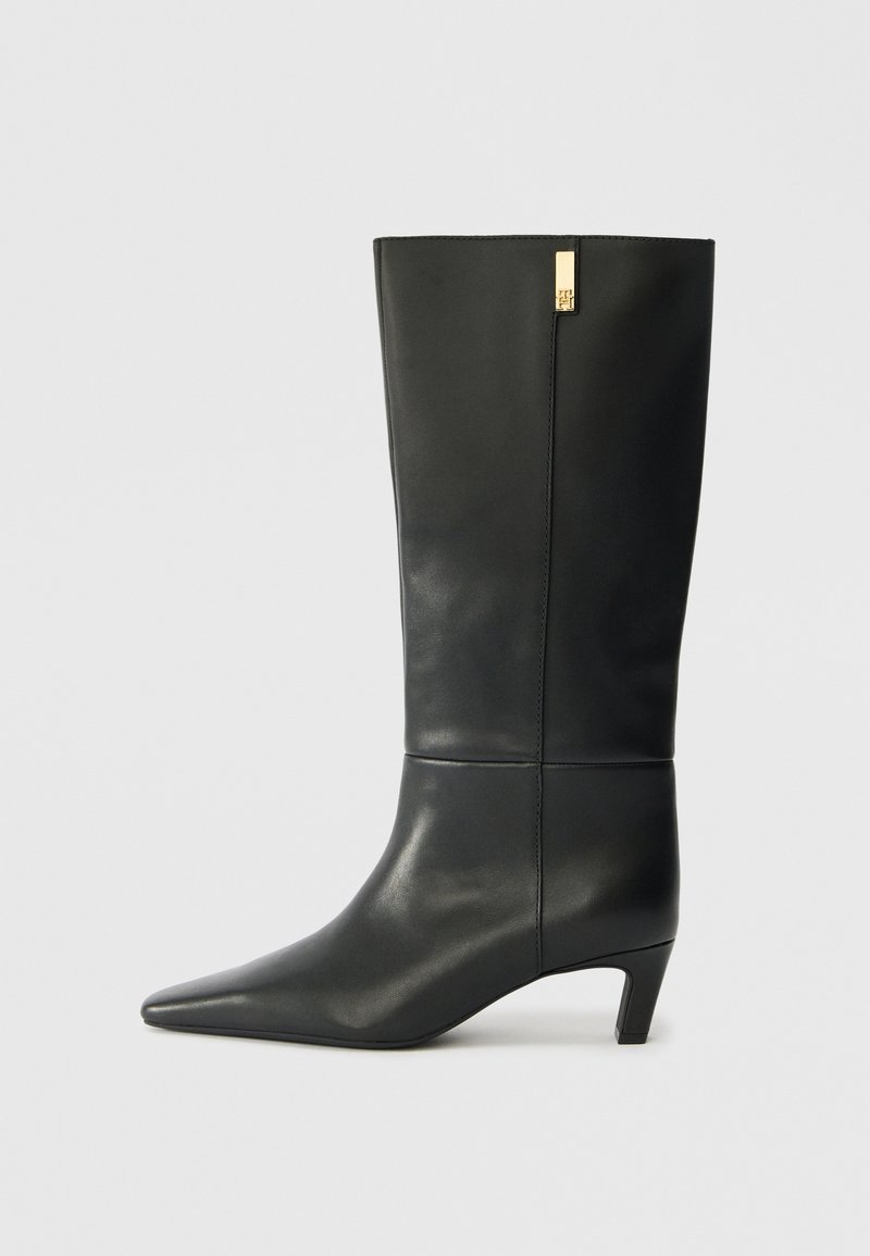 Schwarze Lederstiefelette bis zum Knie mit spitzem Zeh und kleinem Absatz. Hat ein elegantes Design mit goldenen Akzenten. Glatte Textur.