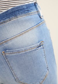 Los pantalones vaqueros de denim azul claro presentan una cintura alta, un bolsillo trasero con costura de contraste y una textura ligeramente desgastada en la tela.
