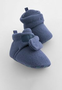 Siniset fleece-tossut, joissa on taitettavat yläosat, teksturoitu kangas ja koristeellinen suljin. Pehmeä pohja mukavuutta varten.