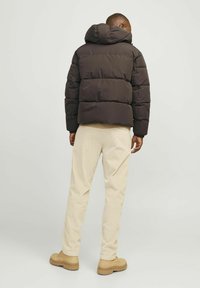 Mørkebrune pufferjakke med en tætsiddende hætte, prydet med et quiltet design. Kombineret med beige fløjlsbukser og brune støvler.