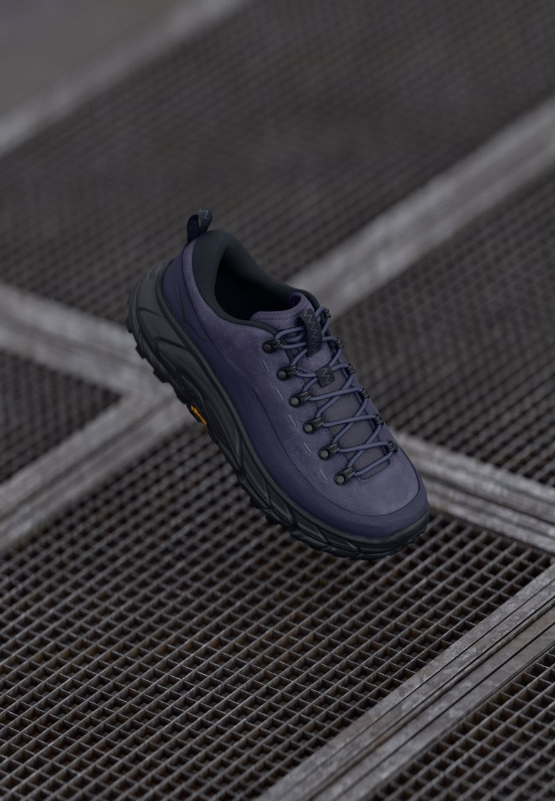 Zapatilla de senderismo morada con un upper texturizado, diseño con cordones, talón acolchado y una suela negra resistente, situada sobre un fondo de rejilla metálica.