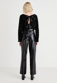 Un haut noir à manches longues en sequins, avec une découpe dans le dos nouée avec des rubans en satin noir. Assorti à un pantalon en cuir verni noir taille haute.