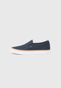 Mornarsko plave slip-on cipele s teksturiranim gornjim dijelom od tkanine, bijelim gumeni potplat i malim crvenim, bijelim i plavim logotipom sa strane.