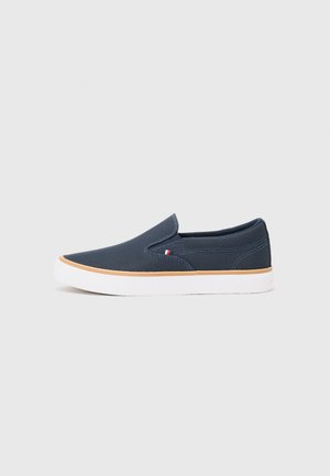 Sapatos slip-on azul-marinho com parte superior em tecido texturizado, sola de borracha branca e um pequeno detalhe de logotipo em vermelho, branco e azul na lateral.
