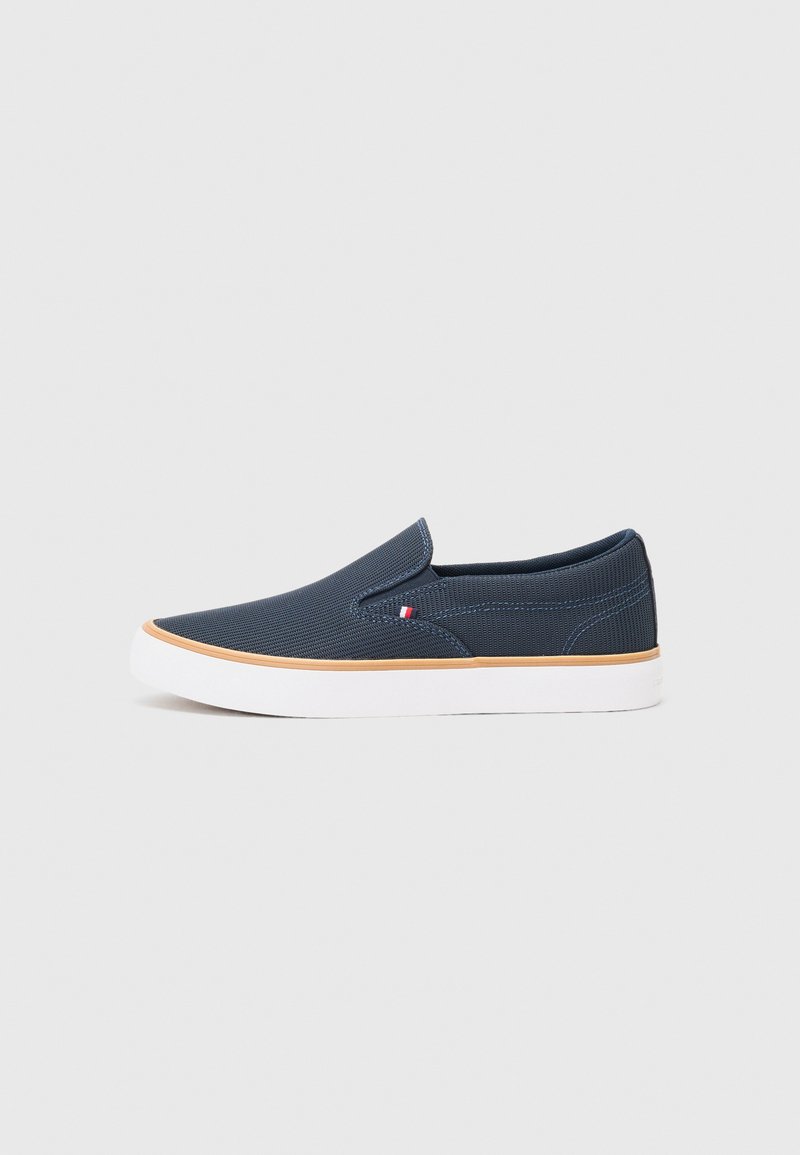 Mornarsko plave slip-on cipele s teksturiranim gornjim dijelom od tkanine, bijelim gumeni potplat i malim crvenim, bijelim i plavim logotipom sa strane.