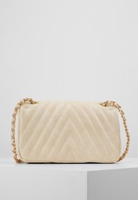 Gep quiltete beigefarbene Lederhandtasche mit einer goldenen Kettenriemen. Rechteckige Form mit Chevron-Muster und minimalistischen Design.