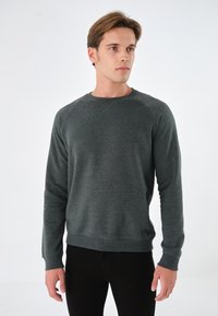 Sudadera de punto gris oscuro con mangas largas, cuello redondo y puños acanalados. Textura suave, diseño minimalista y silueta ajustada.