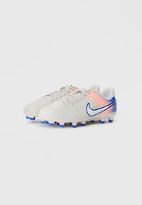 Pair of white soccer cleats with blue studs, blue Nike swoosh, and pink gradient detail on the heel.