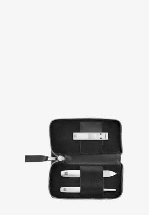 Étui noir zippé contenant trois outils de soin des ongles en métal argenté : coupe-ongles, lime à ongles et pousse-cuticules, disposés horizontalement.