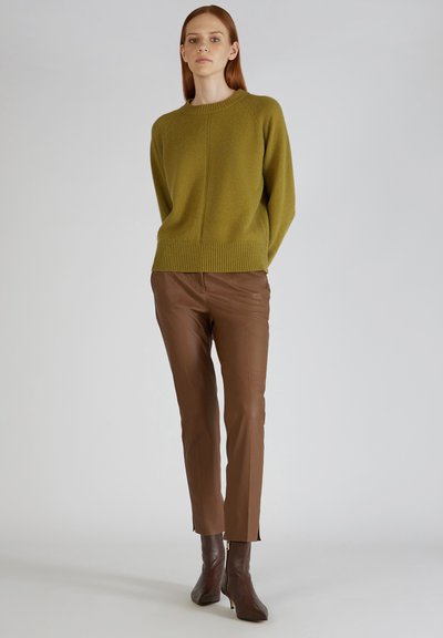 Zielony wełniany sweter z prążkowanym dołem, zestawiony z brązowymi skórzanymi spodniami o slim fit. Model stoi na neutralnym tle.