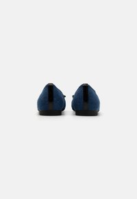 Scarpe slip-on blu in tessuto con accenti neri sul tacco, texture liscia, forma arrotondata e suola nera a profilo basso.