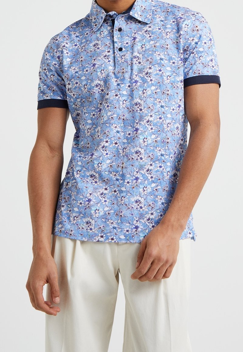 Kortärmad polo-shirt i ljusblått med blommönster, med en tvåknappslåsgång och mörkblå detaljer på kragen och ärmslut.