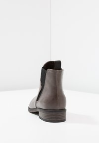 Bottines en cuir marron avec panneaux latéraux en mesh élastique, bout rond et petit talon empilé, présentant un logo embossé subtil à l'arrière.