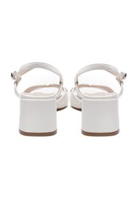 White heeled sandals with a block heel, adjustable ankle strap, and smooth leather material. Design features minimalistic accents and a cushioned insole.