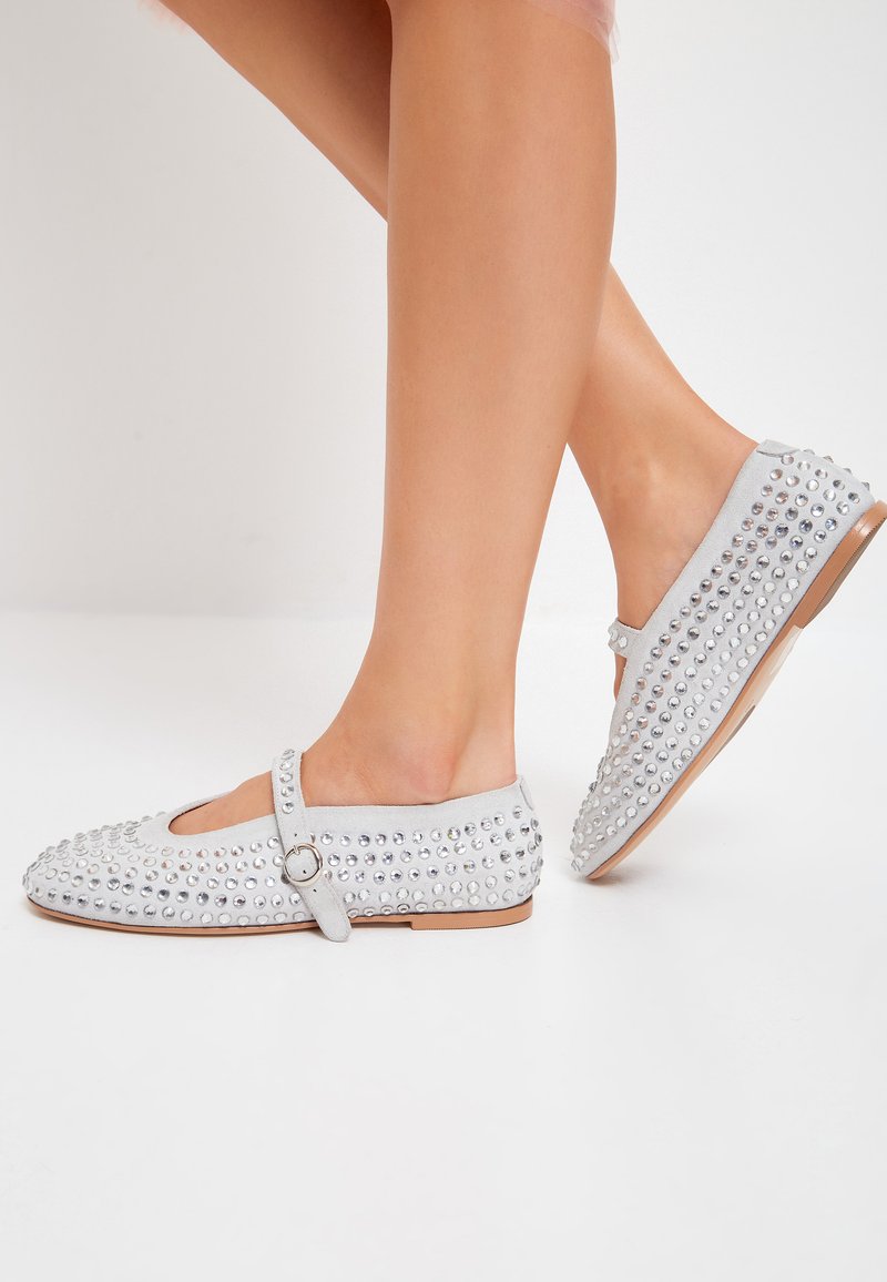 Ballerine con borchie argentate e finitura in morbido suede grigio, dotate di un cinturino alla Mary Jane e un design a punta rotonda.
