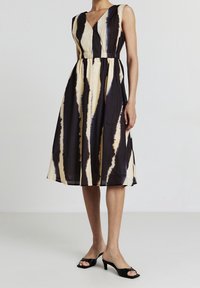 Ärmlös midiklänning med svart och beige vertikala abstrakta ränder, V-ringning, insvängd midja, ihopparad med svarta sandaletter med öppen tå och klack.
