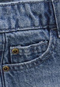 Jeansmaterial med en ljusblå tvätt, som har en framficka med en metallnitar och synliga sömnadsdetaljer. Texturerad yta med ett subtilt mönster.