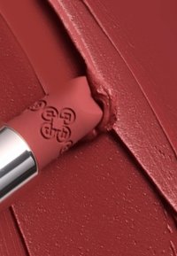 Matowa szminka w delikatnym odcieniu czerwieni, prezentująca gładką teksturę aplikacji. Tubka ma srebrny akcent i wytłaczany wzór dla dodatkowego efektu.