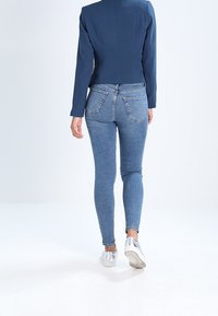 Marinblå croppad kavaj och figursydda blå jeans med bakfickor och smal passform. Silverskor fulländar outfiten.