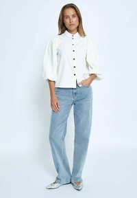 White puff-sleeve shirt with black buttons, structured design, paired with light blue straight-leg jeans and metallic pointed flats.