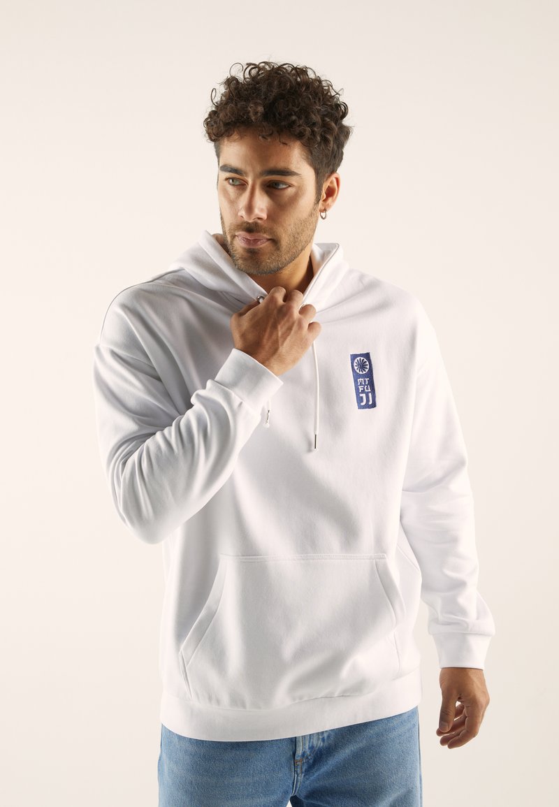 White hoodie with a front pocket and drawstring hood. Features a blue patch with stylized text. Pairing with light blue jeans.