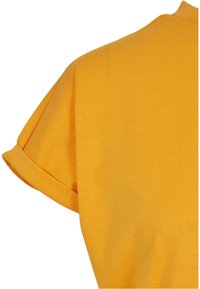 Chemise en tissu de coton jaune moutarde à manches courtes avec un détail de revers roulé sur la manche.