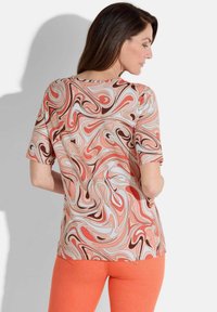 Multicolore top met een spiraalpatroon in koraal, bruin en crème. Korte mouwen, ronde halslijn en een ontspannen pasvorm.