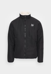 Sort jakke med zip-lukning, høj krave foret med cremet fleece, og et hvidt Puma-logo på venstre bryst. Glat stofstruktur.