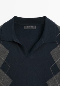 Námořnická modrá polo tričko s šedým argyle vzorem, pletená textura a výstřih do V. Na štítku je napsáno "Massimo Dutti" černým písmem.