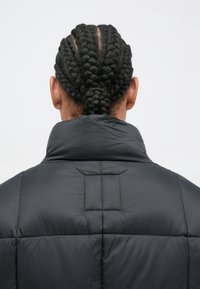 Φουτεράκι σε σκούρο γκρι, με ψηλό γιακά, πλισè ύφανση και ορατές ραφές κατά μήκος των ραφών για πρόσθετη σχεδιαστική λεπτομέρεια.