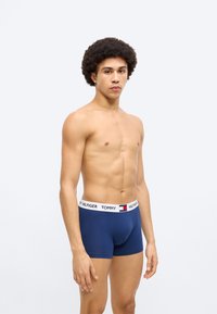 Ανδρικά εσώρουχα boxer σε μπλε ναυτικό χρώμα με λευκή ελαστική ζώνη μέσης που φέρει το λογότυπο "Tommy Hilfiger". Το υλικό φαίνεται λείο και εφαρμοστό.