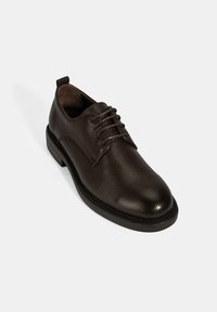 Bruine leren dresschoenen met een gestructureerde afwerking, ronde neus en vetersluiting. Bevat een slanke zool met minimale accenten.