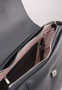 Grå læder messenger-taske med lynlås, der har pink foring, flere rum og sølvfarvede hardware-detaljer.