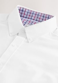 Chemise à col blanc présentant une texture à motif quadrillé bleu et rouge à l'intérieur du col. Boutons et marquage discret près de l'ourlet.